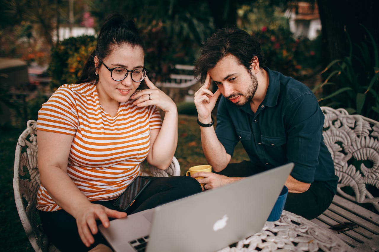 A man and woman sitting on a bench looking at a laptop